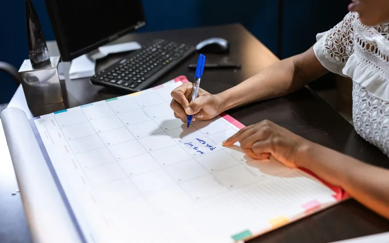 A hand marking dates on a paper calendar with a pen