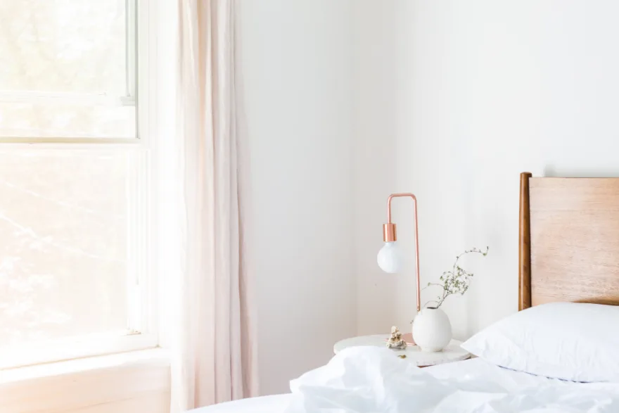 A bedroom with daylight coming through a large window beside the bed in the morning