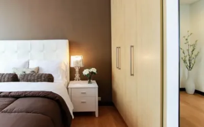A bedroom at night with the bed made and a single warm lamp lit on the bedside table