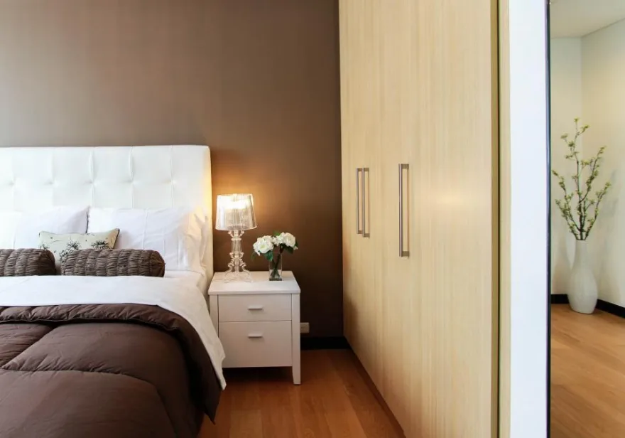 A bedroom at night with the bed made and a single warm lamp lit on the bedside table
